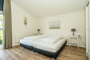 A bedroom with two beds, a window with curtains, a bedside table with a lamp, and a wall art piece. - Holiday home in Renesse with swimming pool (Renesse)