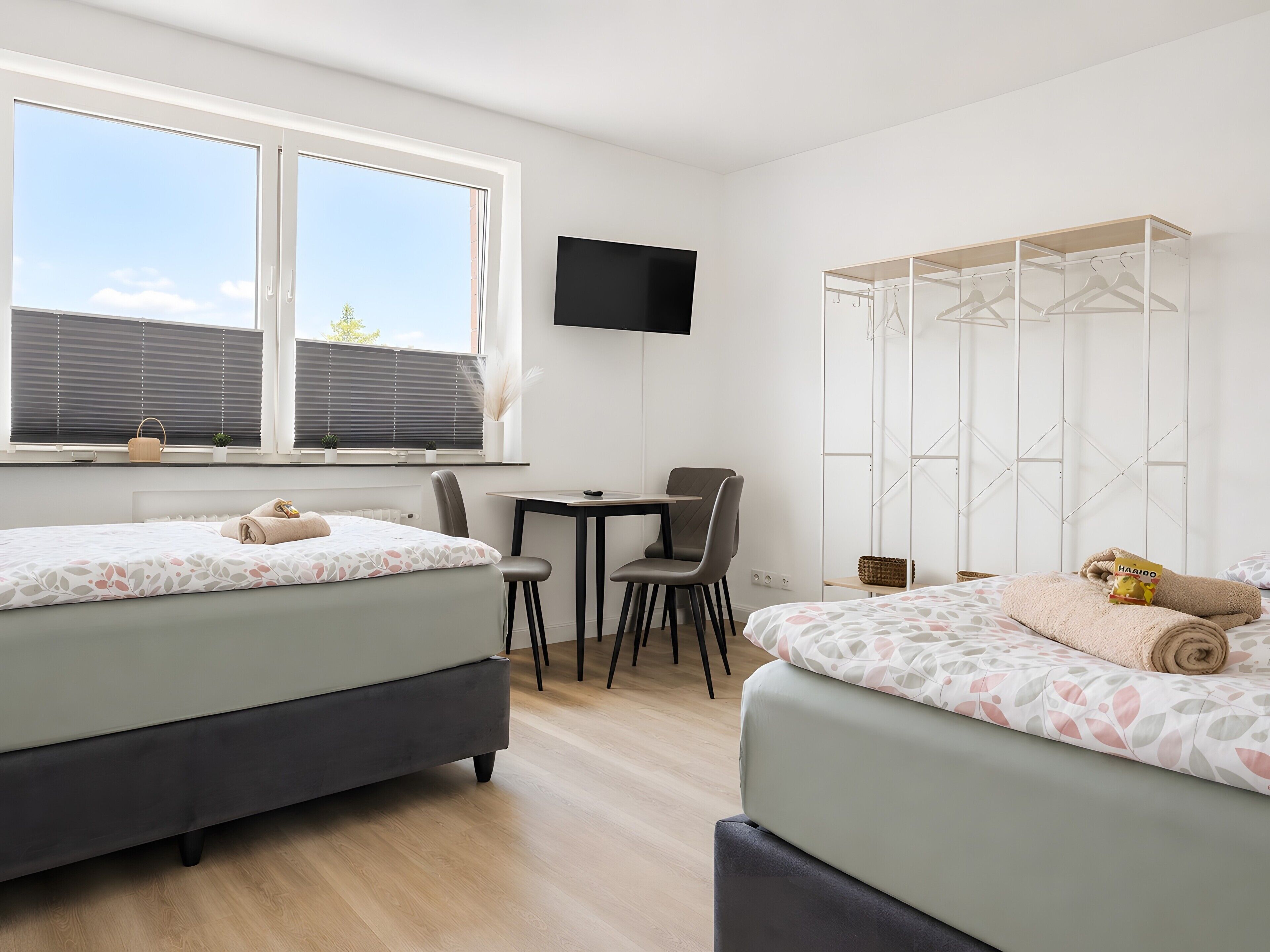 A bedroom with two beds, a desk, a chair, a TV, and a wardrobe.