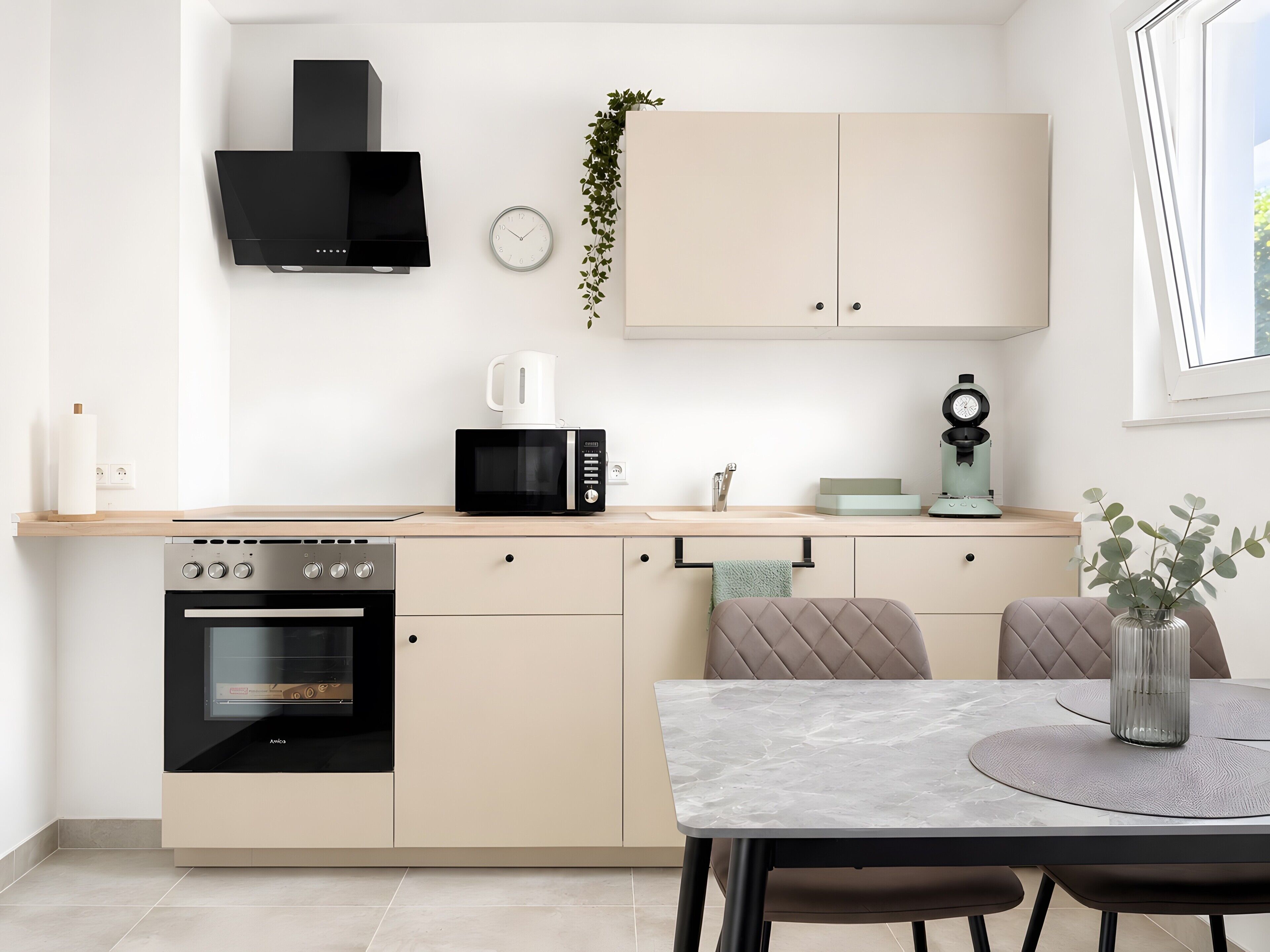 Een moderne keuken met een ingebouwde oven, magnetron en koffiezetapparaat. Er is een eettafel met stoelen en een vaas met bloemen.