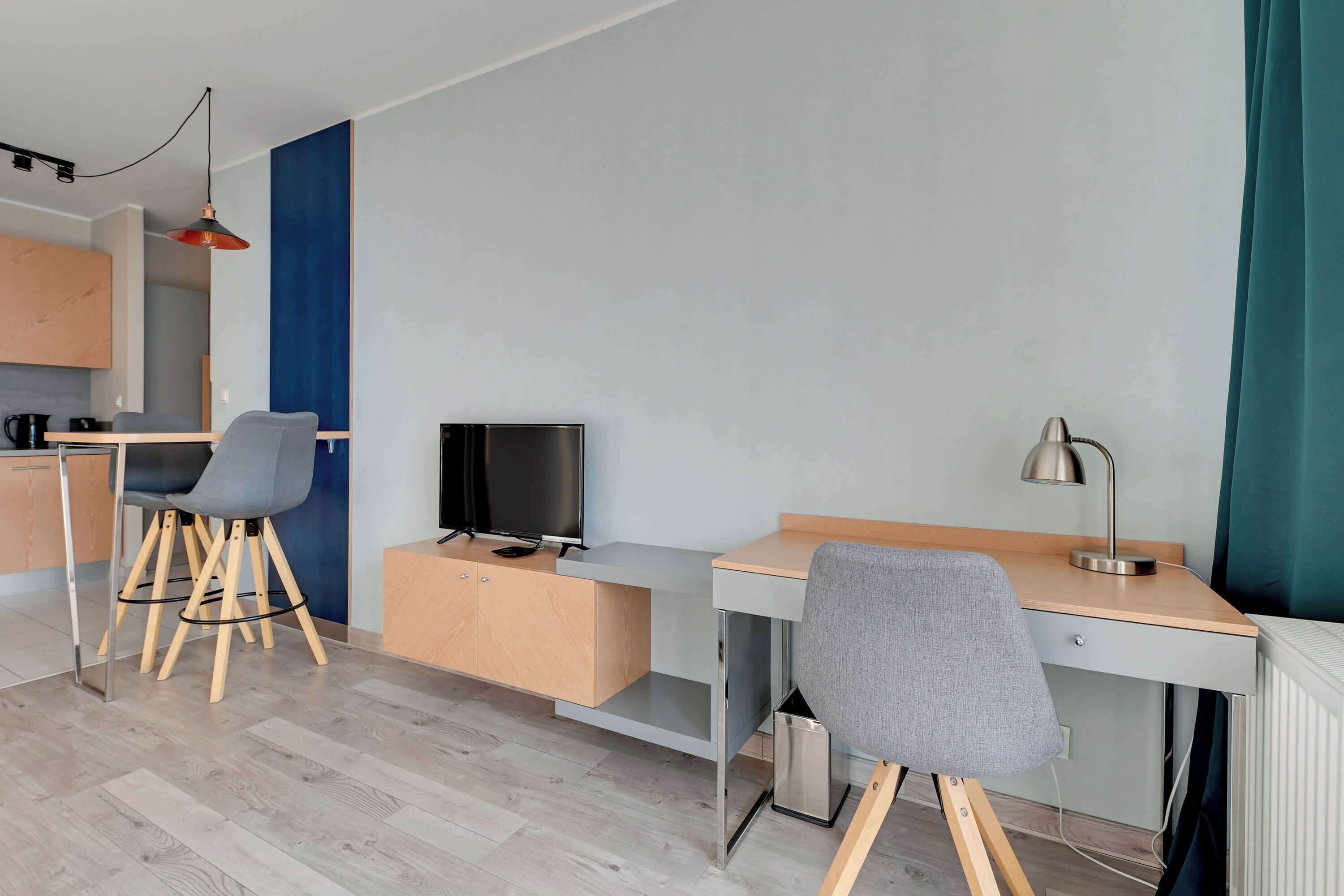 A modern, well-lit room with a desk, chair, and a television.