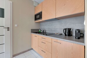 A compact kitchen with wooden cabinets, a microwave, a kettle, and a coffee maker on the countertop.