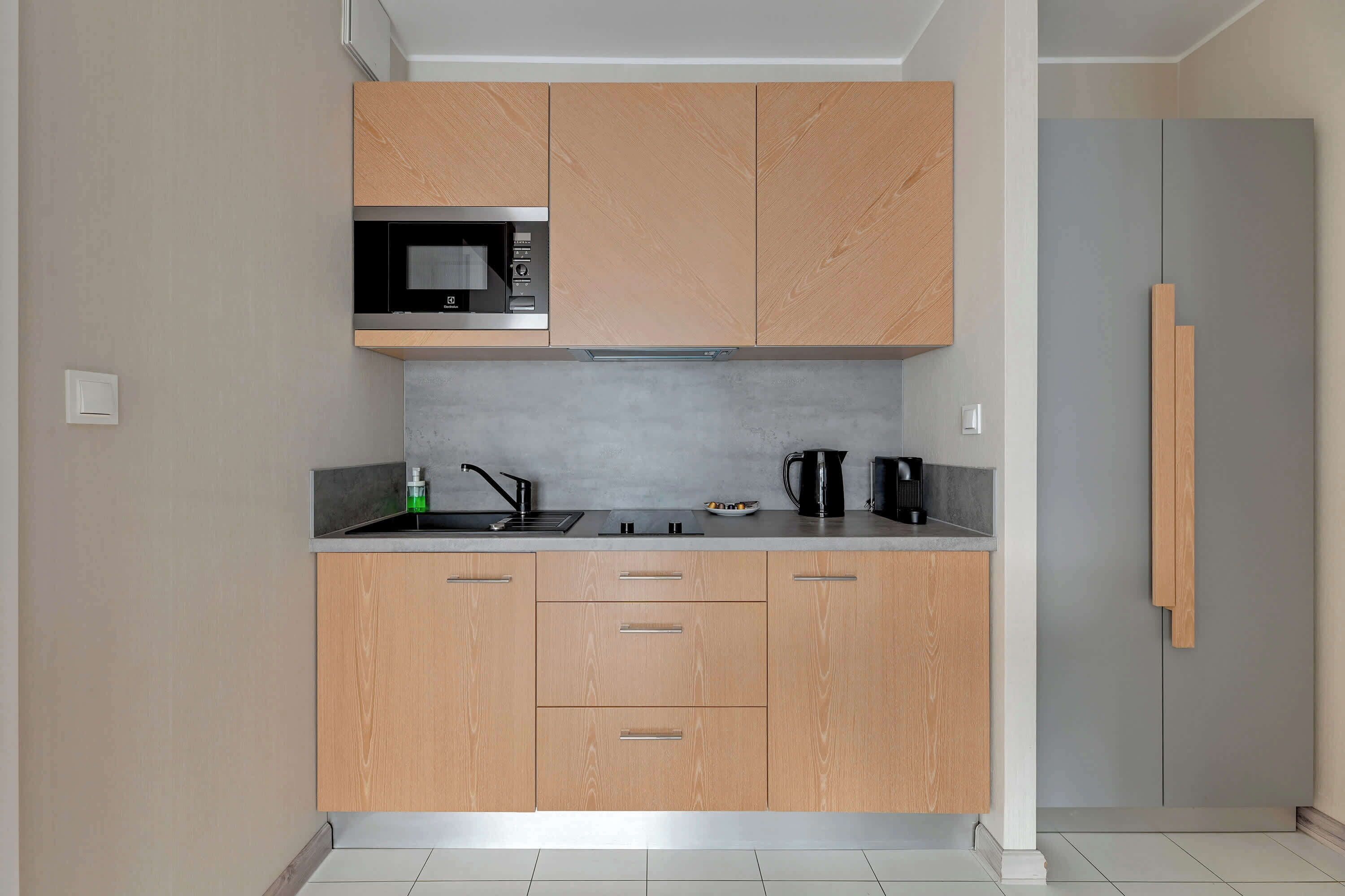 A modern kitchen with wooden cabinets, a microwave, a kettle, and a sink.