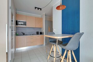 Une cuisine moderne avec des meubles en bois, un four à micro-ondes et un évier. On y trouve une table à manger avec une chaise et une suspension.