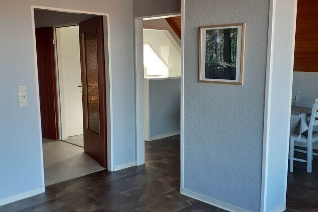 Un couloir avec une porte en bois, un tableau encadré au mur et un escalier en arrière-plan.