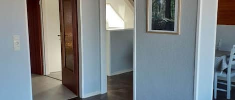 Un couloir avec une porte en bois, un tableau encadré au mur et un escalier en arrière-plan.