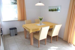 Ein Essbereich mit Tisch, Stühlen, einer Blumenvase, einer Lampe und einem Mülleimer.