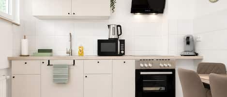 A modern kitchen with white cabinets, a black range hood, a microwave, a coffee machine, and an oven.