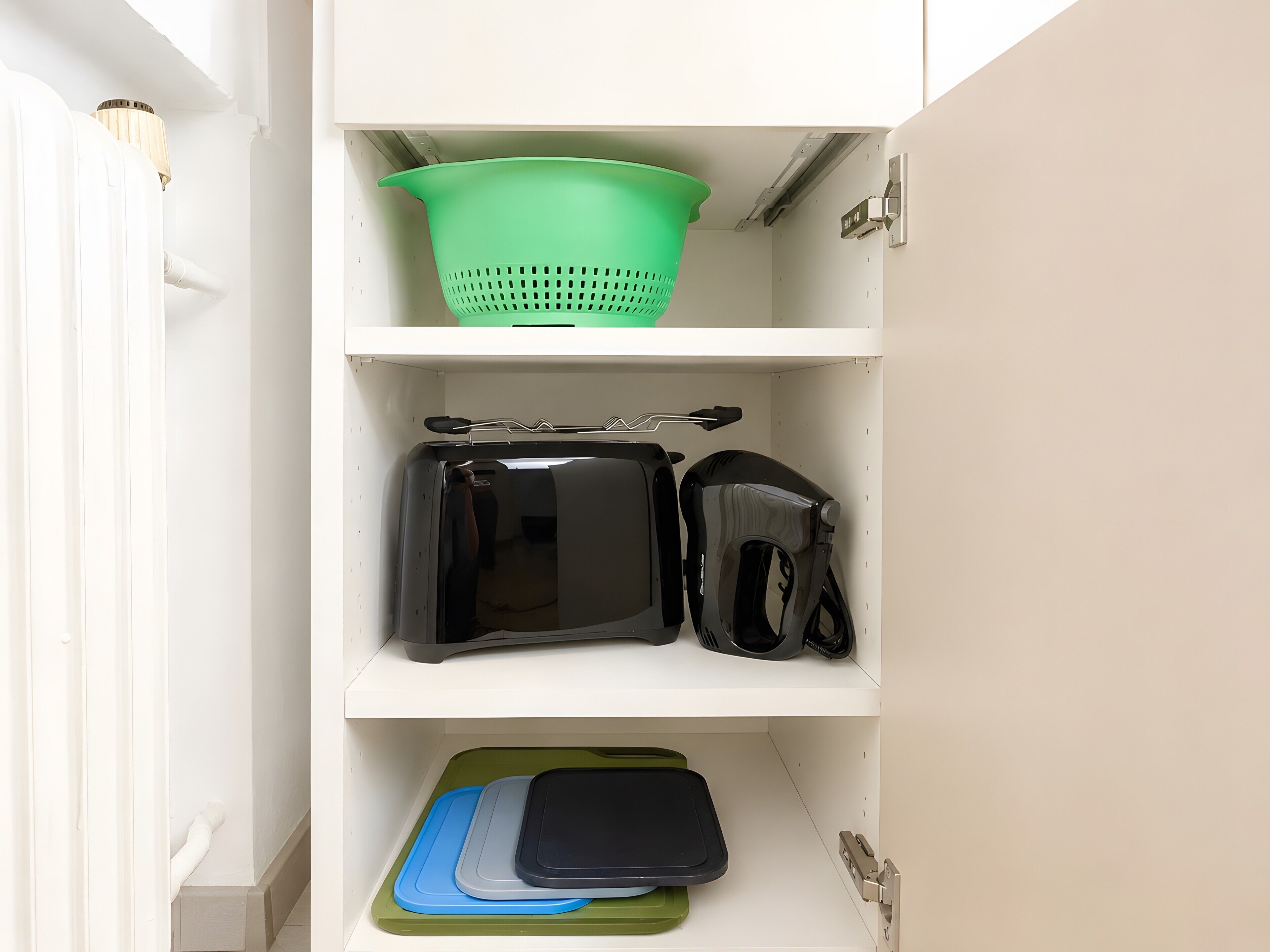 Ein Küchenschrank mit einer grünen Sieb, einem schwarzen Toaster und einer Schneidebrett in Blau und Grün.