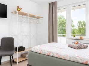 Ein Schlafzimmer mit einem Bett, einem Sessel, einem Kleiderschrank und einem Fenster mit Blick auf Bäume.