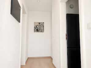 Ein Flur mit einem schwarzen Kühlschrank, einer weißen Tür mit Zebra-Motiv und einem Lichtschalter an der Wand.