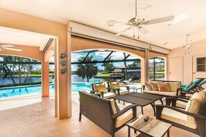 A spacious indoor area with a pool view, outdoor seating, and ceiling fans. - CCVS - Villa Blue Lagoon (Cape Coral)