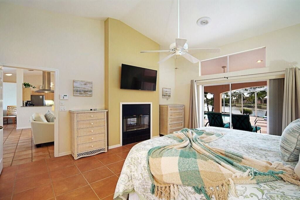 Un dormitorio con cama, televisor, ventilador de techo, chimenea y vistas al exterior.
