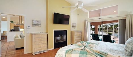 Un dormitorio con cama, televisor, ventilador de techo, chimenea y vistas al exterior.