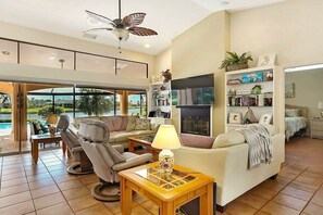A spacious living area with a ceiling fan, a fireplace, a bookshelf, and a view of the outdoors. - CCVS - Villa Blue Lagoon (Cape Coral)