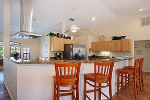 A modern kitchen with a central island, wooden chairs, and a ceiling fan. - CCVS - Villa Blue Lagoon (Cape Coral)