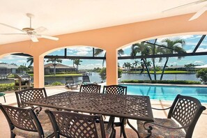 Ein überdachter Außenbereich mit Pool, Stühlen und einem Tisch.