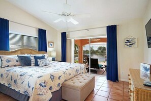 Ein Schlafzimmer mit Bett, Deckenventilator, Fenster mit Vorhängen, Blick ins Freie und einem Essbereich.