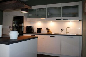 A modern kitchen with white cabinets, a black countertop, and a built-in oven. - Holiday apartment with 1 bedroom (Heeslingen)