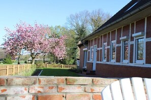 Een gebouw van baksteen met een raam met wit kozijn, een houten hek en een boom met roze bloemen.