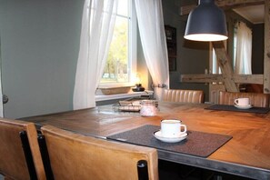 A dining area with a wooden table, chairs, a coffee cup, a candle, and a hanging lamp. - Holiday apartment with 1 bedroom (Heeslingen)