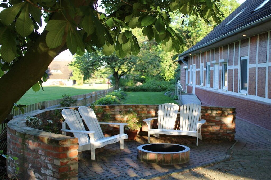 An outdoor seating area with Adirondack chairs and a fire pit, surrounded by brick walls and a brick building in the background.