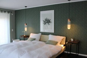 A neatly made bed with white linens and green pillows, a framed artwork above it, and two bedside tables with lamps. - Holiday apartment with 1 bedroom (Heeslingen)