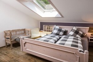 Una camera da letto con una finestra a lucernario, un letto con lenzuola a quadri, una sedia in legno e un comodino con una lampada.