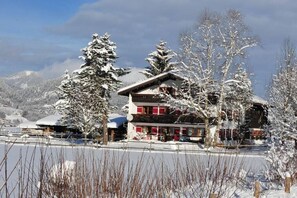 Un edificio a più piani con un tetto spiovente, circondato da alberi imbiancati dalla neve e da montagne sullo sfondo.