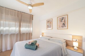 A hotel room with a bed, a ceiling fan, two bedside tables with lamps, and two framed artworks on the wall.