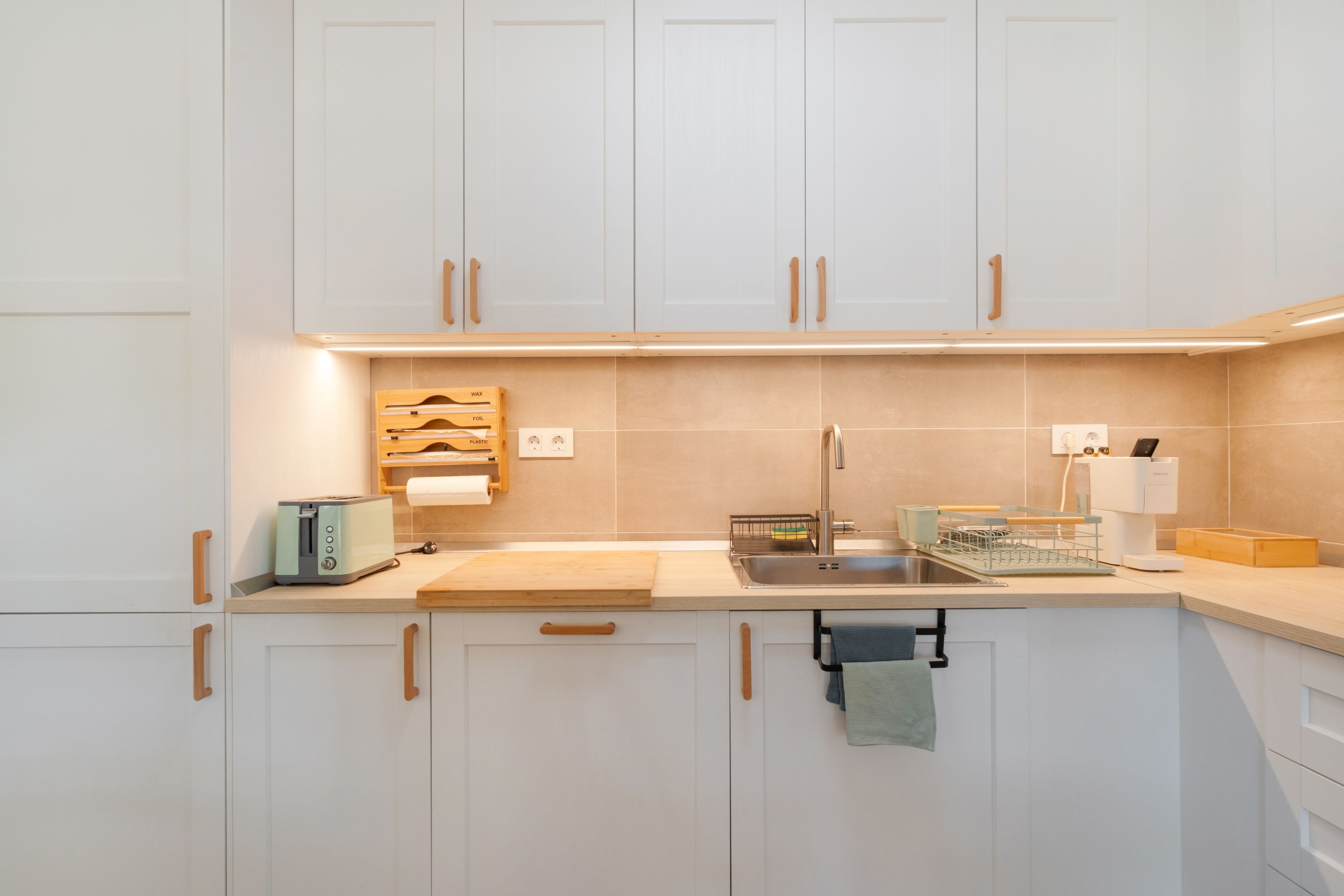 Eine moderne Küche mit weißen Schränken, einer Edelstahl-Spüle und einer Holzausziehtafel.