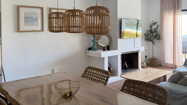 A dining area with a wooden table, wicker chairs, and hanging wooden light fixtures.