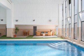 An indoor swimming pool with a lounge area, including a sofa and chairs, and a door leading to another room.