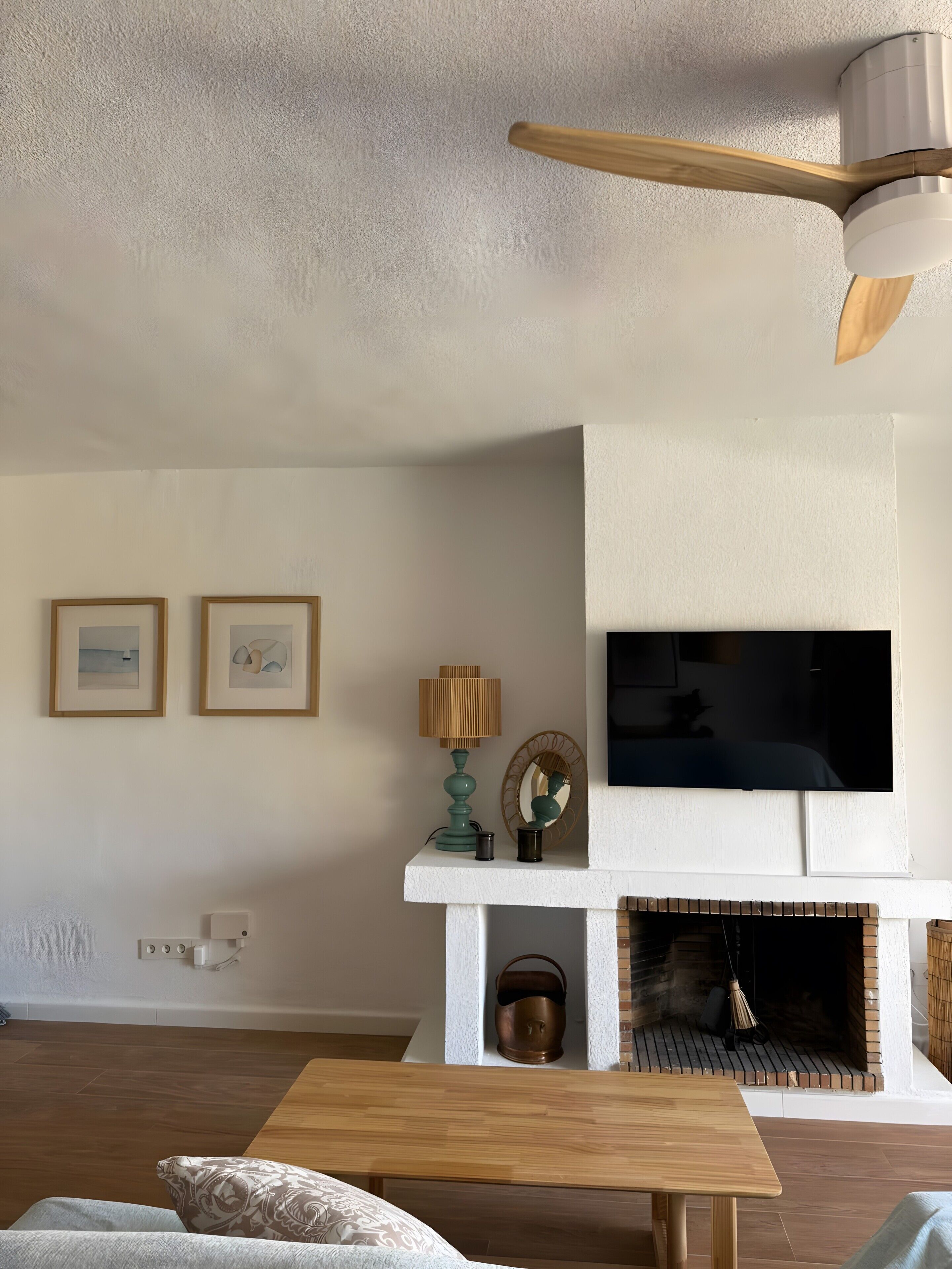 Ein Wohnzimmer mit Kamin, einem flachbildfernseher darüber, einem Deckenventilator und einem Holztisch.