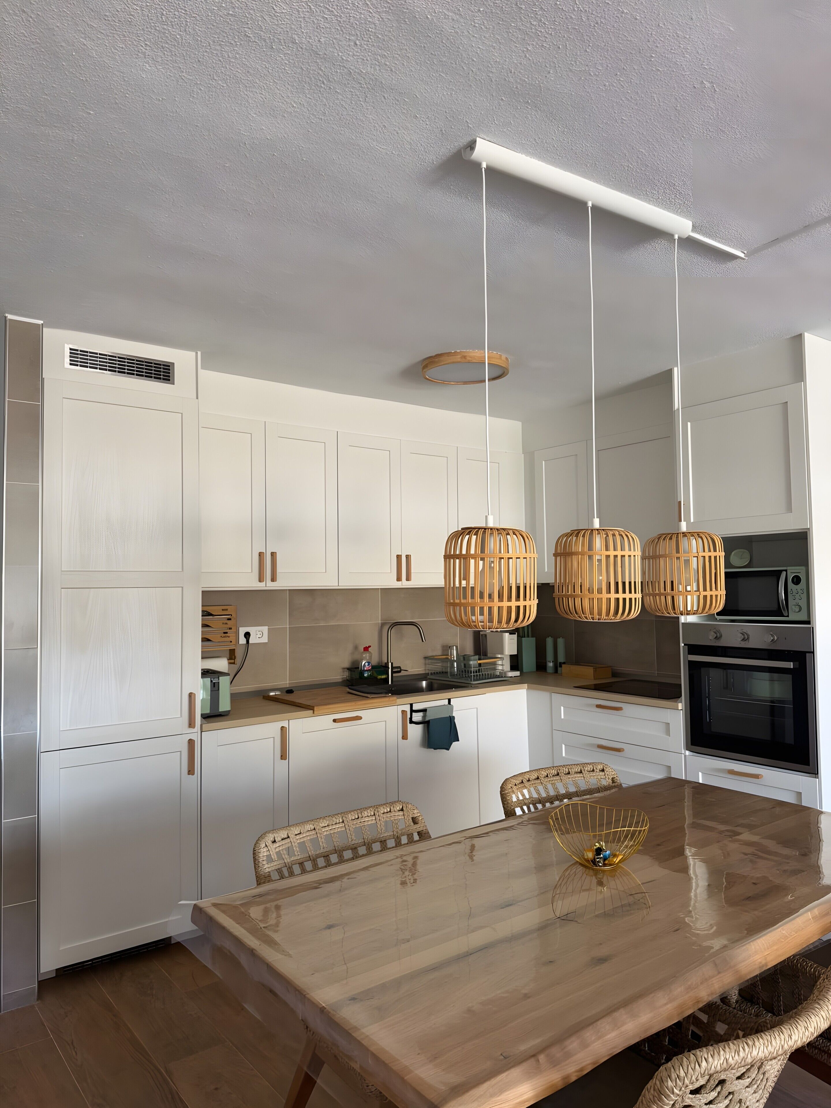 A modern kitchen with white cabinetry, a wooden dining table, wicker chairs, and a built-in oven.