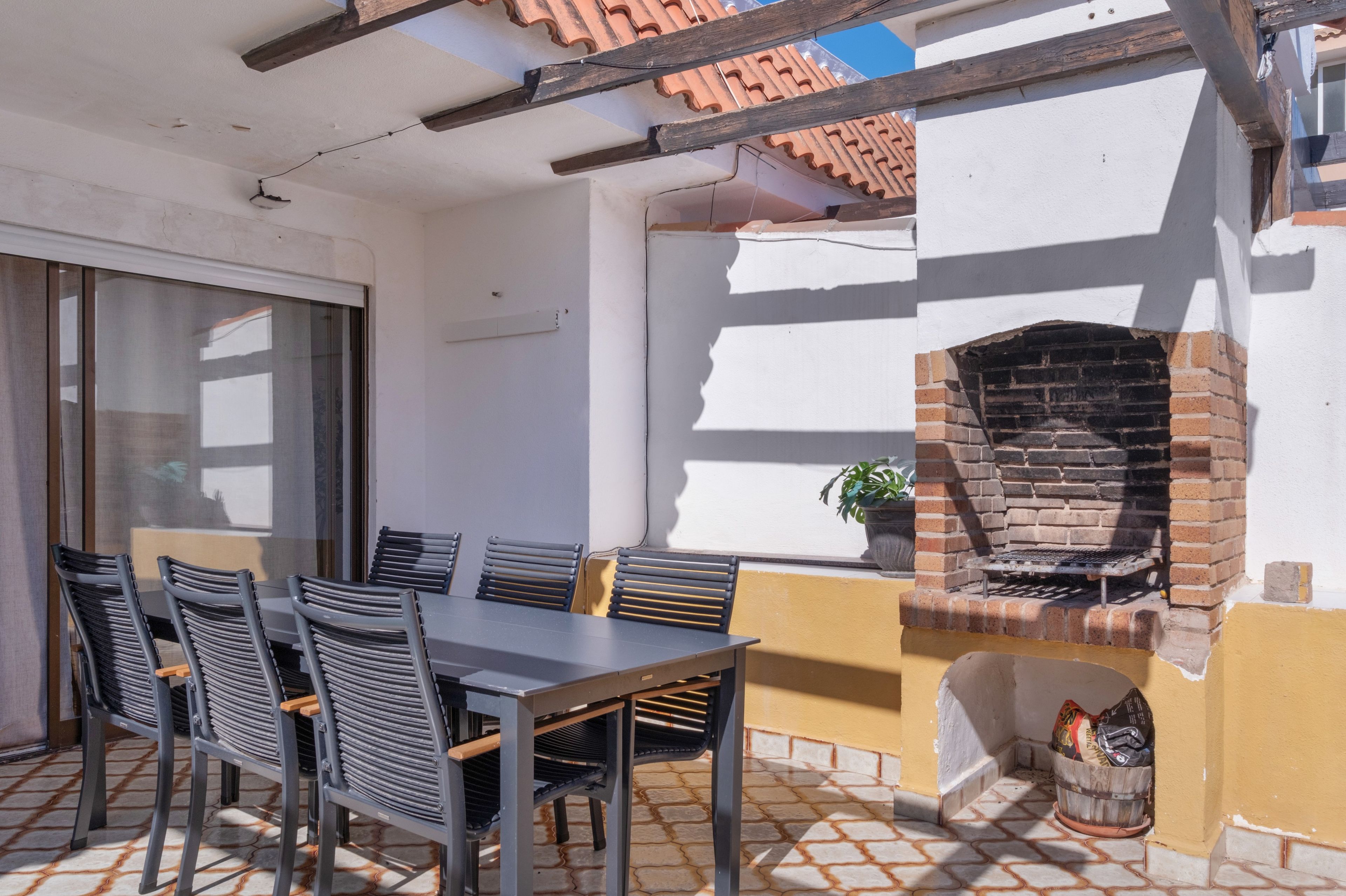 Une terrasse extérieure avec un four en briques, une table avec des chaises et une fenêtre.