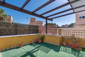 Une terrasse sur le toit agrémentée d’une pergola en bois, d’un gazon synthétique vert et de plantes en pot.