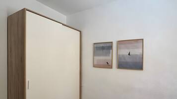 Una habitación con un armario de madera, un ventilador de techo y dos cuadros en la pared.