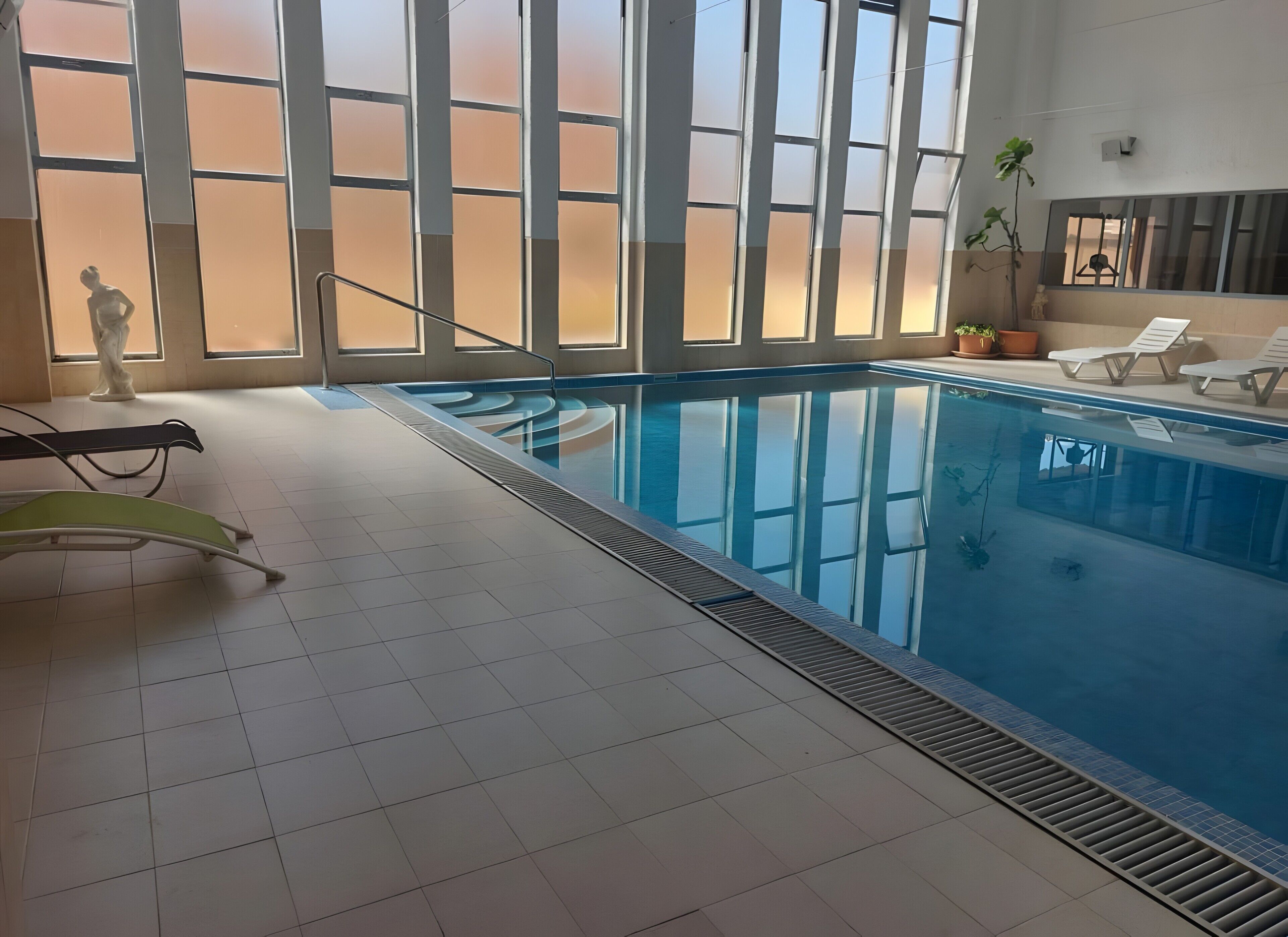 Ein Innenpool mit großen Glaswänden, gefliestem Boden und Liegestühlen am Pool.