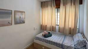 A room with a bed, a ceiling fan, a window with curtains, and two framed pictures on the wall.
