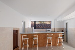 Een moderne keuken met een bar, witte barkrukken en uitzicht op een betegeld dak.
