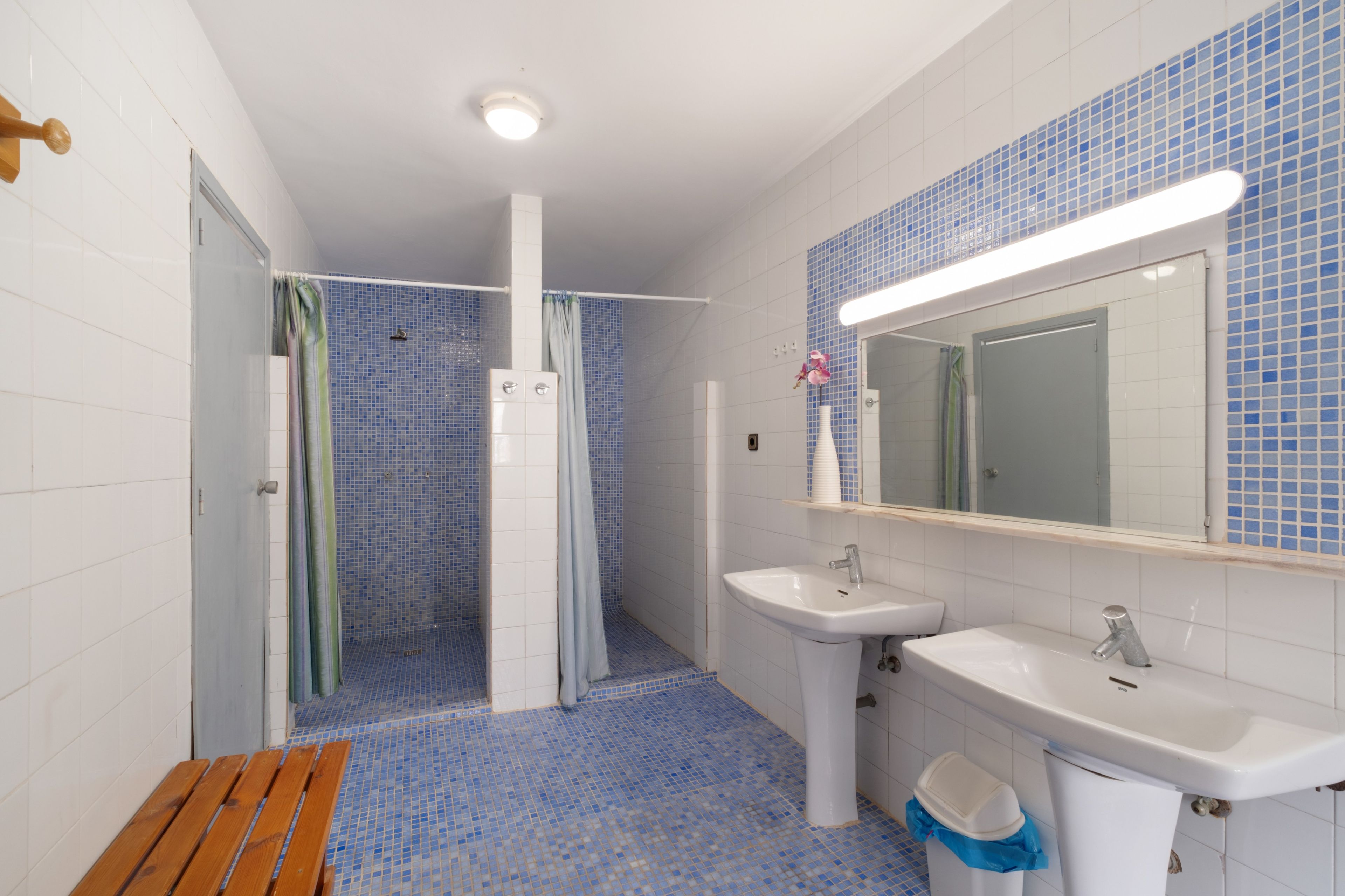 Ein Badezimmer mit Dusche, zwei Waschbecken, einem Spiegel und einer hölzernen Bank.