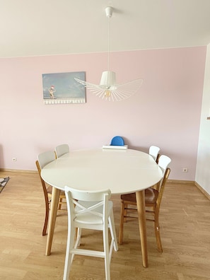 Une table de salle à manger ronde, entourée de six chaises, un luminaire suspendu blanc et un tableau au mur.