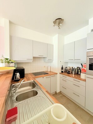 A modern kitchen with white cabinets, a wooden countertop, stainless steel sink, and various appliances. - Lovely Apartment for 6 Guests with Beautiful Water Views Baby Cot Included (Knokke-Heist)