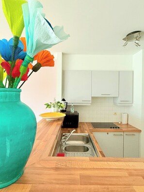 Une cuisine avec des plans de travail en bois, un évier et des armoires blanches. Un vase rempli de fleurs en papier colorées est posé sur le plan de travail.