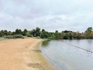 A sandy beach with a calm water body, a child playing, and a line of trees in the background. - Lovely Apartment for 6 Guests with Beautiful Water Views Baby Cot Included (Knokke-Heist)