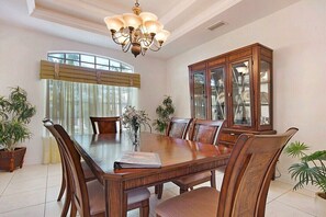 Une salle à manger avec une grande table en bois, des chaises, un lustre et un buffet aux portes vitrées.