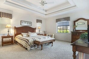 Ein Schlafzimmer mit einem großen Bett, zwei Nachttischen, einem Sessel, einem Schreibtisch und einem Deckenventilator.