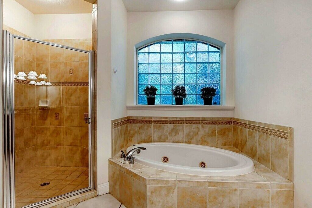 A bathroom with a walk-in shower, a freestanding bathtub, and a window with potted plants.