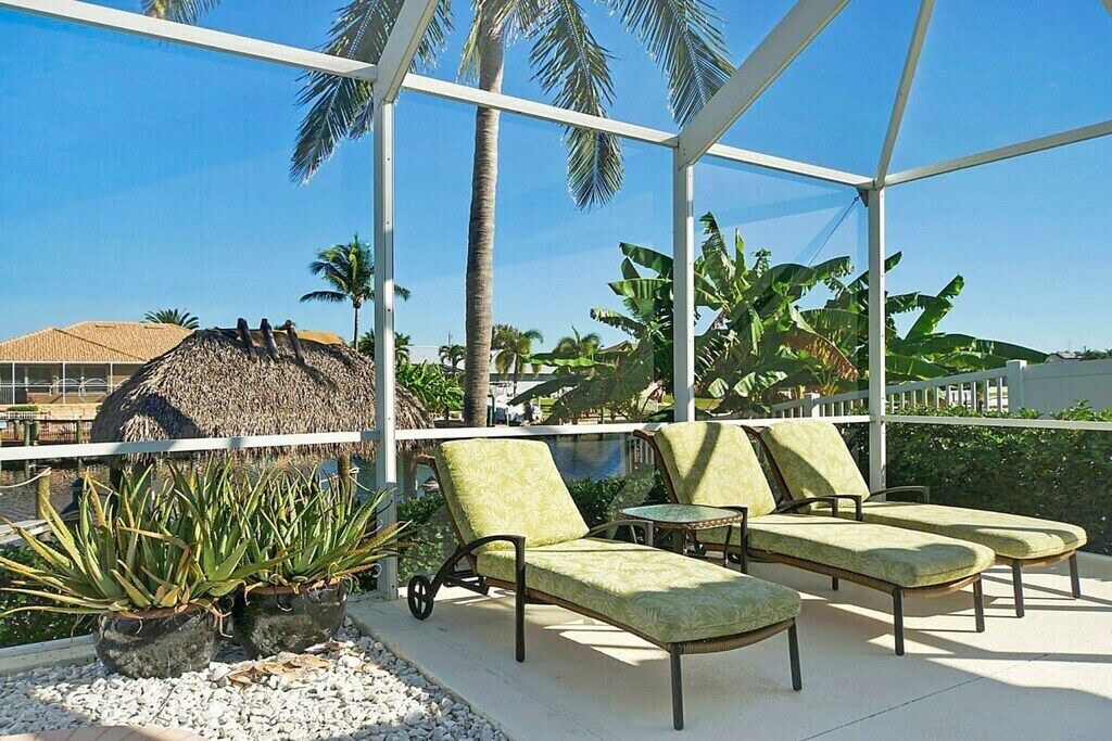 A covered outdoor seating area with lounge chairs and a thatched structure in the background.