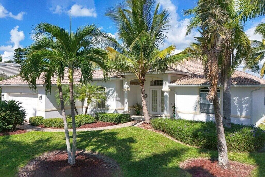 A residential house with a white exterior, a tiled roof, and a well-maintained lawn with palm trees.